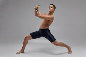 foto di un' bello uomo balletto ballerino, vestito nel un' nero corti, fabbricazione un' danza elemento contro un' grigio sfondo nel studio.