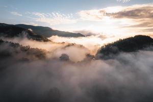 il sole sorge nella nebbia e nelle montagne al mattino foto
