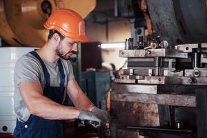 ritratto di un giovane lavoratore con un elmetto in un grande impianto di lavorazione dei metalli. l'ingegnere serve le macchine e produce parti per apparecchiature a gas foto