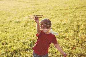 bambino felice nel casco pilota che gioca con un aeroplano giocattolo di legno e sogna di diventare volante