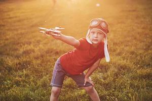 bambino felice nel casco pilota che gioca con un aeroplano giocattolo di legno e sogna di diventare volante foto