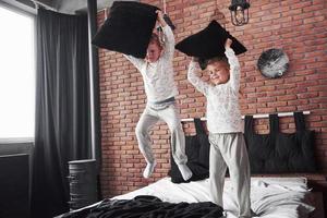bambini cattivi ragazzino e ragazza hanno messo in scena una battaglia di cuscini sul letto in camera da letto. a loro piace quel tipo di gioco foto