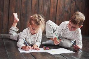 i bambini si sdraiano sul pavimento in pigiama e disegnano con le matite. bambino carino dipinto con le matite foto