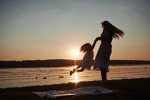 la mamma gioca con il suo bambino in vacanza vicino all'oceano, sagome al tramonto foto