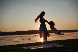 la mamma gioca con il suo bambino in vacanza vicino all'oceano, sagome al tramonto foto