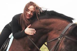 giovane ragazza carina che abbraccia il suo cavallo mentre è seduto a cavalcioni. le piacciono gli animali foto