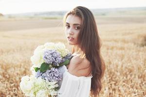 bella ragazza in abito bianco che corre sul campo di grano autunnale all'ora del tramonto foto