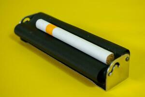 un' nero metallo rullo per rendere sigaretta, sigaretta rullo fatto a mano su giallo sfondo foto