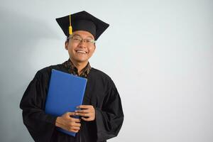 espressive di adulto Indonesia maschio indossare la laurea veste, cappello e occhiali, asiatico maschio la laurea portare vuoto blu certificato isolato su bianca sfondo, espressioni di ritratto la laurea foto