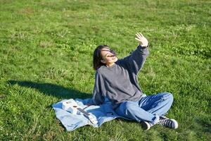 contento asiatico ragazza seduta su picnic coperta con ukulele, copertina se stessa a partire dal luce del sole, estendendosi mano in direzione sole travi e sorridente foto