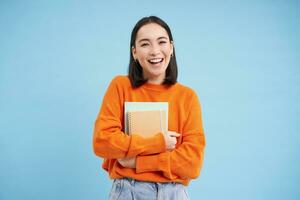 sorridente asiatico donna con i Quaderni, alunno con contento viso, promo di Università formazione scolastica, blu sfondo foto