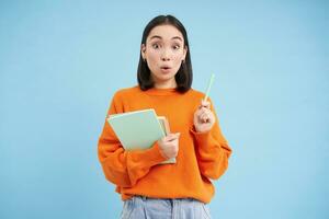 sorridente asiatico donna con i Quaderni, alunno con contento viso, promo di Università formazione scolastica, blu sfondo foto