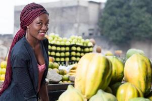 sorridente giovane donna in piedi tra scaffali di frutta. foto