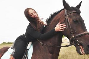 giovane ragazza carina che abbraccia il suo cavallo mentre è seduto a cavalcioni. le piacciono gli animali