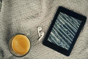 lettore di e-book, una tazza di caffè e un auricolare foto