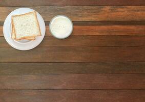 pane nel un' piatto. latte nel un' bicchiere su un' di legno tavolo. foto