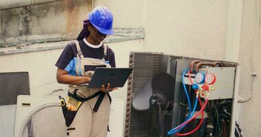 qualificato africano americano elettricista Lavorando su al di fuori HVAC sistema, Tenere il computer portatile. concesso in licenza tecnico addetto alla manutenzione ottimizzazione esterno aria condizionatore prestazione, garantendo esso opera a massimo capacità foto