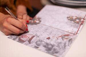 avvicinamento di fidanzata mani scrittura natale saluto carta per famiglia durante Natale vacanza in piedi nel natale decorato cucina. contento famiglia godendo la spesa inverno stagione insieme foto