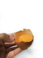 un' donna di mano crepe un uovo per separato il uovo bianca e tuorlo e il uovo conchiglia nel il sfondo. foto