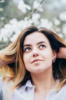 una bella ragazza in un giardino gode di alberi in fiore guardando sognante verso l'alto foto