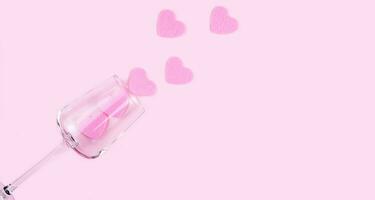 creativo flatlay composizione con rosa cuori e bicchiere di vino su il rosa sfondo. San Valentino giorno concetto. superiore Visualizza. copia spazio. selettivo messa a fuoco. foto