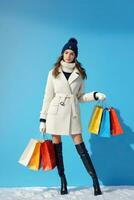 ai generato un' sorridente giovane donna nel inverno capi di abbigliamento Tenere shopping Borsa isolato su blu sfondo foto