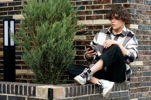 giovane uomo legge qualcosa su il Telefono mentre seduta su il mattone frenare foto
