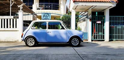 bangkok, Tailandia - settembre 29, 2023 blu e bianca classico mini bottaio parcheggiata su il strada nel davanti di le case Ingresso porta con luce del sole. vecchio veicolo, mezzi di trasporto e Vintage ▾ auto concetto. foto