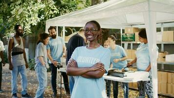 ritratto di africano americano signora indossare bicchieri al di fuori con braccia attraversato e occhi fisso su telecamera. a cibo viaggio, volontari siamo aiutando il povero, bisognoso e senza casa le persone. zoom indietro, palmare. foto