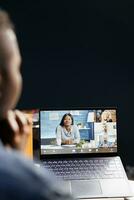 africano americano donna video conferenza con colleghi a casa. femmina libero professionista collaboratore in linea e discutere opera utilizzando un' il computer portatile nel un' vivente camera ufficio impostare. foto