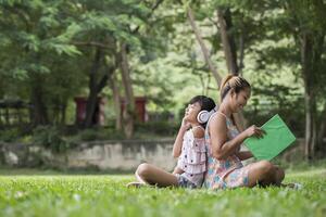 madre e figlia che leggono una favola a sua figlia ascoltano il suono con le cuffie nel parco foto