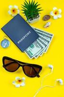 accessori flatlay per le vacanze estive. pianificazione del viaggio. passaporto, denaro, occhiali da sole su sfondo giallo.