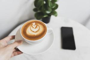 mano che tiene latte o cappuccino con schiuma schiumosa, vista dall'alto della tazza di caffè nella caffetteria. foto