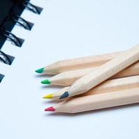 primo piano di cinque matite di legno colorate disposte su un blocco note bianco. materiale scolastico
