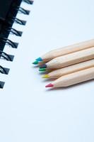 primo piano di una pila di matite colorate in legno disposte su un blocco note bianco. sei elementi.