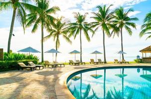 bellissimo ombrellone di lusso e sedia intorno alla piscina all'aperto in hotel e resort con palme da cocco su cielo blu foto