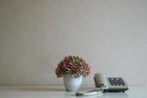 telefono e vaso di fiori sulla scrivania sullo sfondo del muro grigio foto