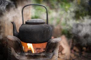 far bollire l'acqua vecchio bollitore sul fuoco con una stufa a carbone su sfondo sfocato foto