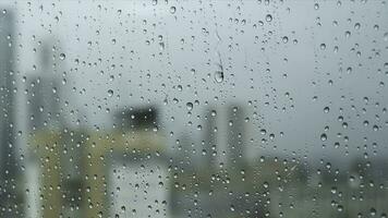 vicino su di un' bicchiere finestra su un' piovoso giorno con grande gocce su sfocato città ang grigio pesante cielo sfondo. azione filmato. trasparente acqua gocce su un' verticale bicchiere superficie. foto