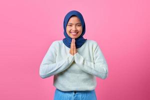 ritratto di giovane donna asiatica sorridente che mostra gesto di preghiera su sfondo rosa