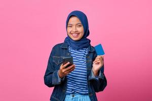 ritratto di giovane donna asiatica sorridente che tiene smartphone mentre mostra la carta di credito