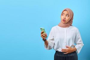 ritratto di giovane donna asiatica scioccata con la bocca aperta che tiene il telefono cellulare mentre guarda di lato foto