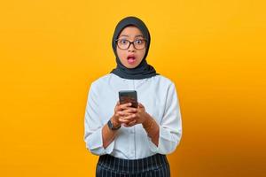 sorpresa giovane donna asiatica che tiene il telefono cellulare con la bocca aperta su sfondo giallo