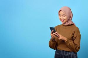 felice giovane donna asiatica che utilizza un telefono cellulare e guarda lo schermo dello smartphone su sfondo blu
