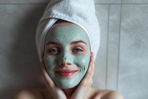 ai generato sorridente giovane donna con asciugamano su testa l'applicazione facciale maschera nel bagno foto