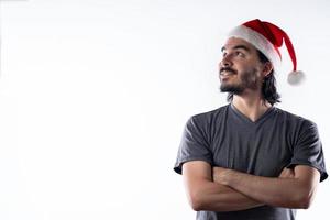 ritratto di uomo latino sorridente con cappello di Natale che guarda di lato con le braccia incrociate. sfondo bianco foto