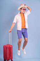 giovane uomo asiatico che tiene la valigia rossa su sfondo blu