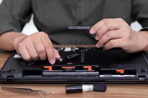 un' uomo hold difficile disco con Cacciavite nel mano riparazione il computer portatile computer aggiornare e pulizia e attrezzo computer riparazione su il tavolo foto