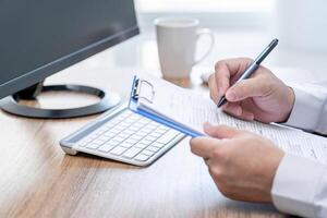 un' uomo uso penna Scrivi su documento di auto riparazione e uso del desktop computer Lavorando e caffè tazza su tavolo nel ufficio foto