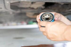 vicino su mano un' uomo hold vecchio olio filtro sotto auto su sollevamento per auto Manutenzione concetto foto